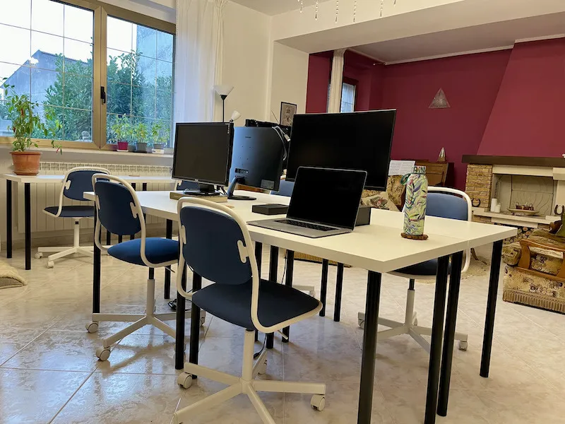 The spacious sitting room of the La Vita Sukha villa displaying a comfortable coworking workstation with 6 desks, 6 ergonomic chairs, and computer monitors.